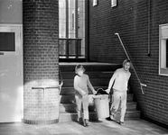 855081 Afbeelding van een twee leerlingen die een vuilnisbak buiten gaan zetten in het gebouw van de Thorbecke ...